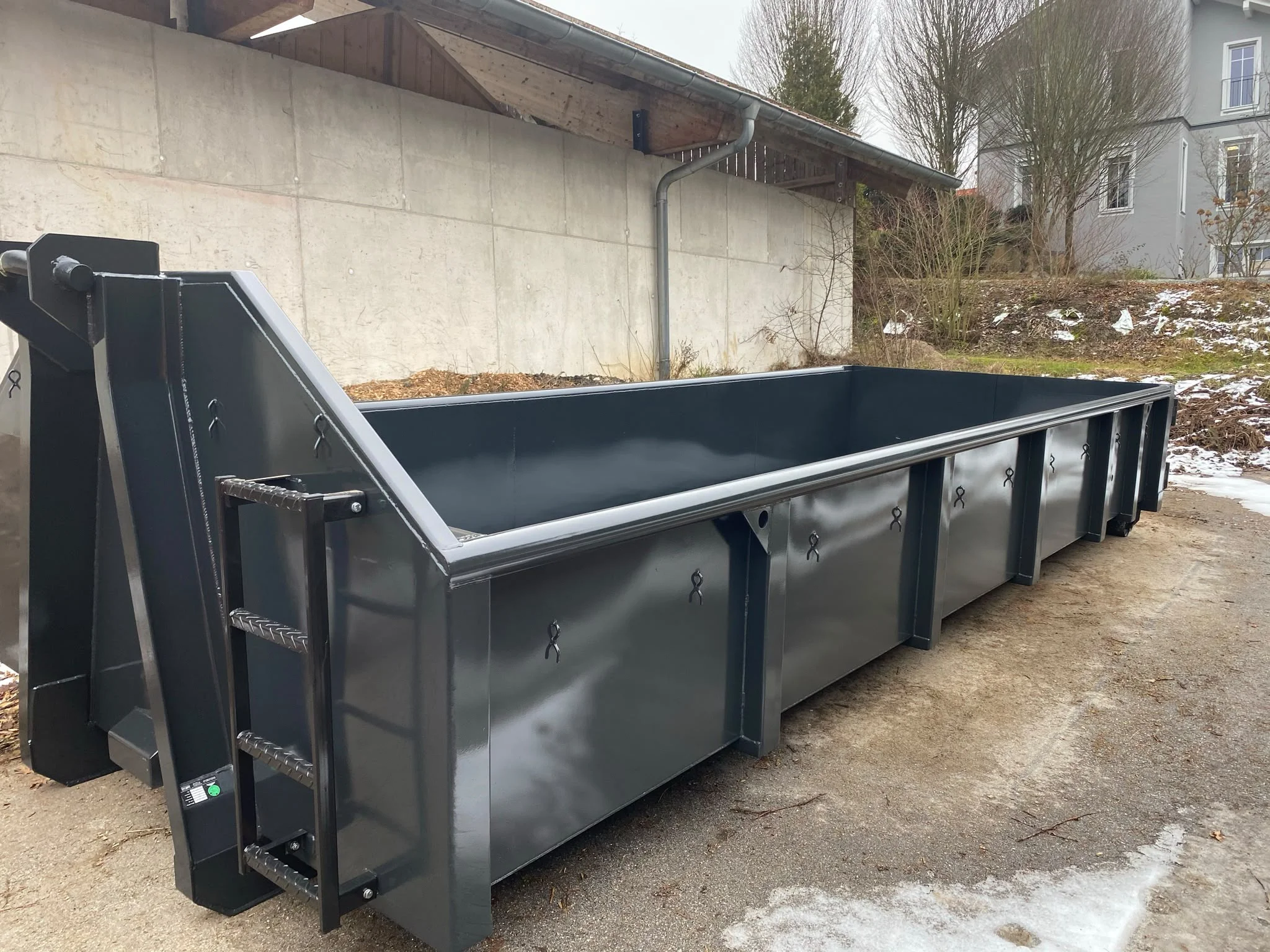 Flacher anthrazitfarbener Abrollcontainer mit Leiter und Hakenaufnahme