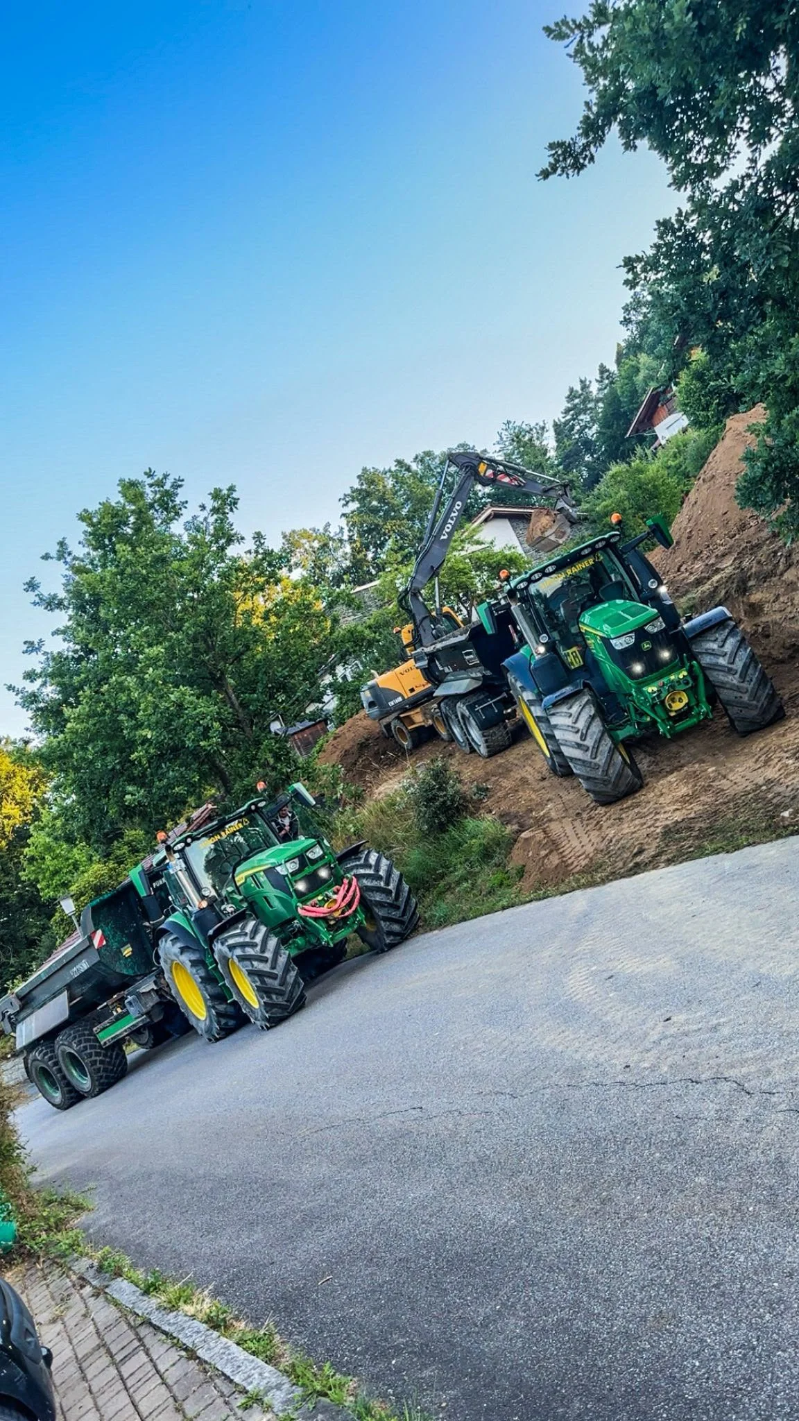 Zwei John-Deere-Traktoren mit Erdmulden beim Beladen durch einen Bagger
